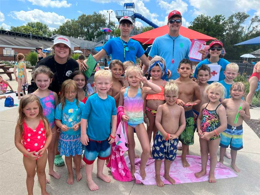 Group of children in concession stand with lifeguards posing for a picture.